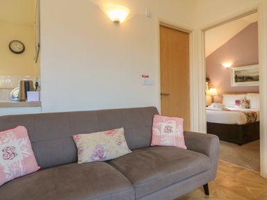 A living room with a gray sofa and cushions next to a doorway leading to a bedroom at Chalet Log Cabin L12 Combe Martin