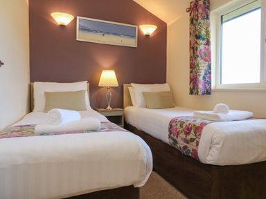 A bedroom with two single beds bedside table lamp and window with floral curtain at Chalet Log Cabin L14 in Combe Martin
