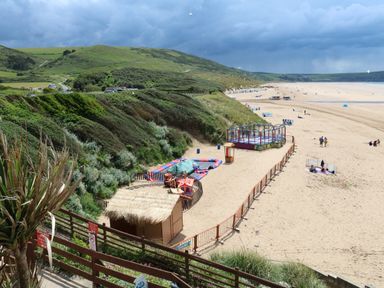 A sandy beach with a small fenced play area and green hills in the background at Chalet Log Cabin L14 in Combe Martin