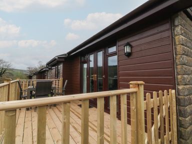 A wooden deck with a table and chairs outside a brown wooden building at Chalet Log Cabin L14 in Combe Martin