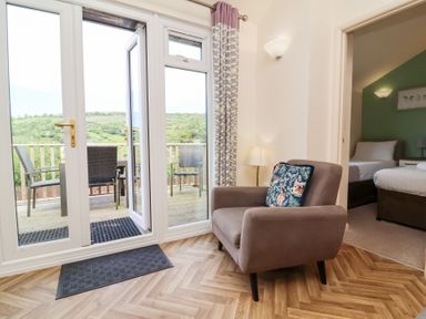 A living area with an armchair and glass doors opening to a balcony with chairs at Chalet Log Cabin L14 in Combe Martin