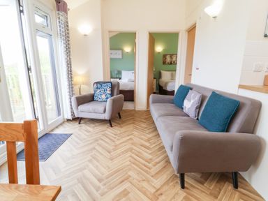 A living room with a sofa and armchair facing two bedrooms at Chalet Log Cabin L14 in Combe Martin