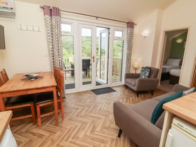 A living room with dining table and chairs sofa armchair and glass doors leading to a balcony at Chalet Log Cabin L14 in Combe Martin