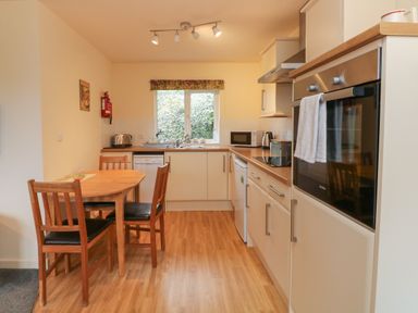 A kitchen with a wooden dining table and chairs a dishwasher oven microwave and sink at Larchwood Lodge in Combe Martin