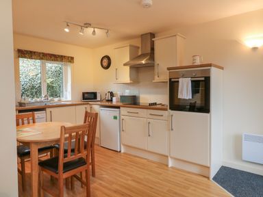 A kitchen with wooden dining table and chairs white cabinets and appliances at Larchwood Lodge in Combe Martin