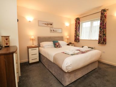 A bedroom with a bed two bedside tables with lamps floral curtains and framed pictures at Larchwood Lodge in Combe Martin