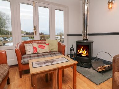 A sitting area with a leather sofa, wooden tables, a wood-burning stove, and glass doors at Chalet Lodge (Bunks) L1 in Combe Martin