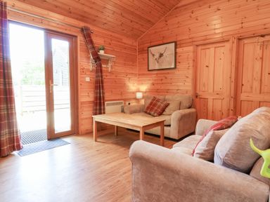 A living room with a wooden coffee table two beige sofas and curtains by a glass door at Chalet Lodge Bunks L1 in Combe Martin
