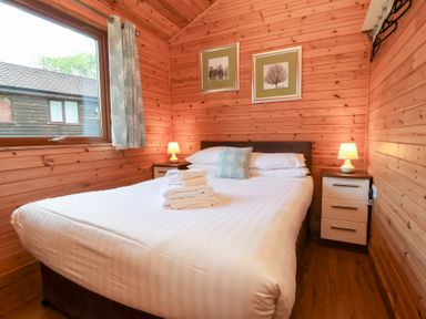 A bedroom with a double bed bedside tables lamps and framed pictures on wooden walls at Chalet Lodge Bunks L1 in Combe Martin