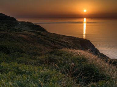 A sunset over the ocean with hills and a path at 1 Manleigh Park Combe Martin
