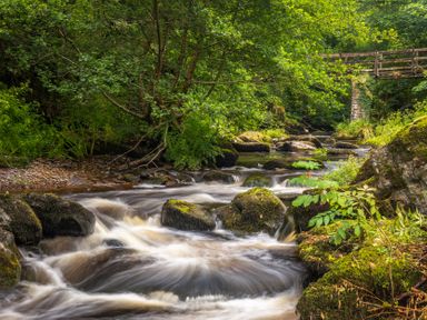 A river flowing over rocks with a wooden bridge in the background