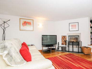 A living room with a white sofa with red pillows a television and a fireplace at Great Brightor Cob Barn in St Kew Highway
