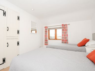 A bedroom with two single beds orange pillows white cupboards and patterned curtains at Great Brightor Cob Barn in St Kew Highway