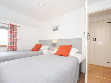 A bedroom with two single beds with gray bedspreads and orange pillows at Great Brightor Cob Barn in St Kew Highway
