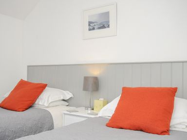 A bedroom with two single beds with orange pillows and grey bedding at Great Brightor Cob Barn in St Kew Highway