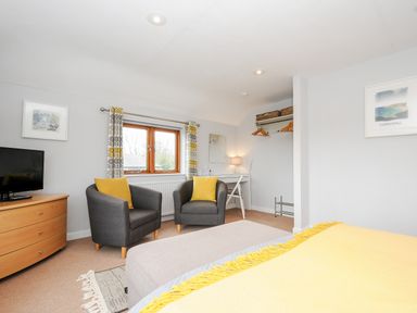 A bedroom with two armchairs and yellow cushions a wooden dresser with a television and a desk with a lamp at Great Brightor Cob Barn in St Kew Highway