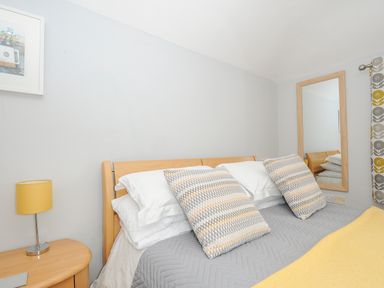 A bedroom with a bed with patterned pillows a bedside table lamp a wall mirror and a framed picture at Great Brightor Cob Barn in St Kew Highway