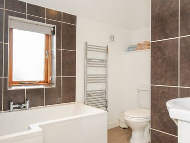 A bathroom with a bathtub a window a toilet a towel rack and shelves with towels at Great Brightor Cob Barn in St Kew Highway