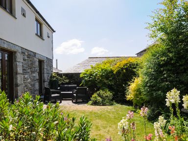 A garden with outdoor seating furniture and flowering plants next to a stone house at Great Brightor Cob Barn in St Kew Highway