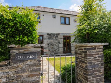 A stone gate with a metal gate leading to a house with stone and white walls at Great Brightor Cob Barn in St Kew Highway