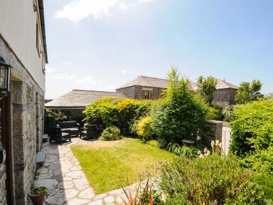 A garden with outdoor seating and stone buildings in the background at Great Brightor Cob Barn in St Kew Highway