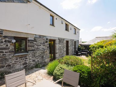 An outdoor patio area with chairs and a table next to a stone and plaster house at Great Brightor Cob Barn in St Kew Highway