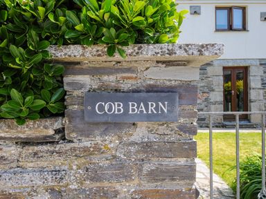 A stone wall with a sign that says cob barn and green bushes at Great Brightor Cob Barn in St Kew Highway
