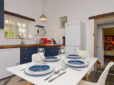 A kitchen with a dining table set for four with blue plates near a white refrigerator at Great Brightor Cob Barn in St Kew Highway