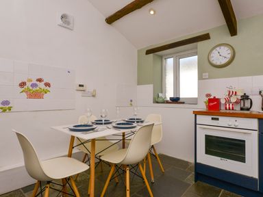 A dining area with a table set for four and an oven under a window at Great Brightor Cob Barn in St Kew Highway