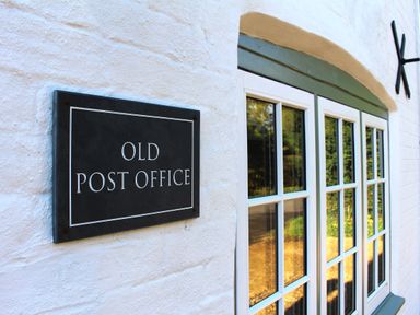White wall with a black sign reading OLD POST OFFICE next to a window with multiple glass panes at Old Post Office Sherborne