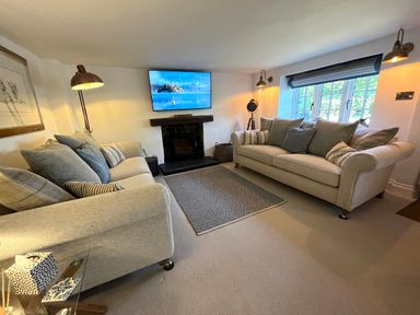 A living room with two sofas a TV above a fireplace and a window with blinds at Old Post Office in Sherborne