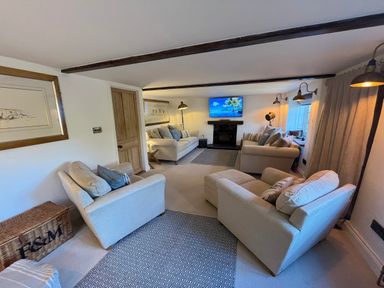 A sitting room with three beige sofas a patterned rug a television above a fireplace and wooden beams on the ceiling at Old Post Office in Sherborne