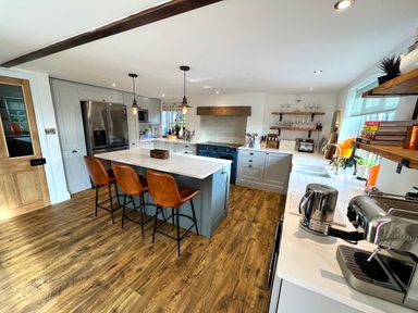 A kitchen with a wooden floor a central island with three chairs stainless steel appliances and shelves with books at Old Post Office Sherborne