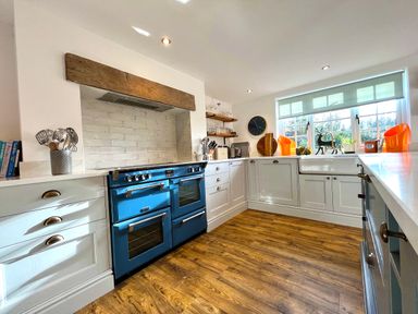 A kitchen with a blue oven a wooden floor white cabinets and a window at the Old Post Office in Sherborne