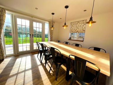 A dining room with a long wooden table black chairs pendant lights and glass doors at Old Post Office in Sherborne