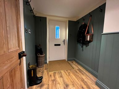 An entrance hall with a white door wooden floor and hooks on green paneled walls holding a jacket and bag at Old Post Office in Sherborne