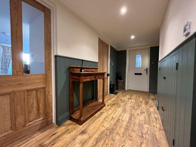 A hallway with wooden flooring a wooden console table coat hooks and a white door at Old Post Office in Sherborne