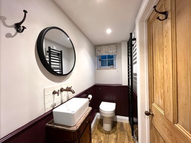 A bathroom with a wooden door a rectangular sink a round mirror a toilet and a small window at Old Post Office in Sherborne