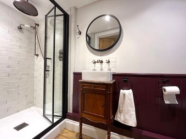 A bathroom with a glass shower enclosure and a wooden vanity with a rectangular sink and round mirror at Old Post Office in Sherborne