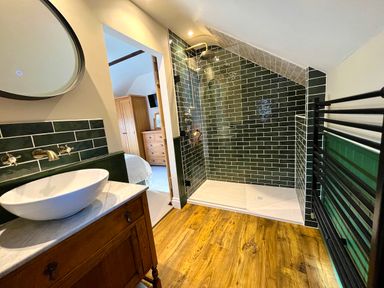 A bathroom with a walk-in shower with green tiles wooden floor and a wooden vanity at Old Post Office in Sherborne
