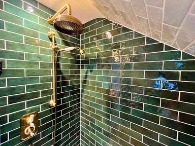 A shower area with green rectangular tiles and brass shower fixtures at Old Post Office in Sherborne