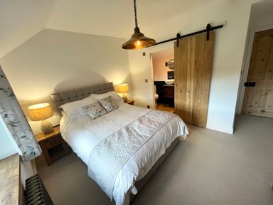 A bedroom with a double bed bedside tables lamps and a sliding wooden door leading to a bathroom at Old Post Office Sherborne