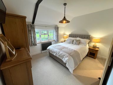 A bedroom with a double bed two bedside tables with lamps a window with curtains and a wooden wardrobe at Old Post Office in Sherborne