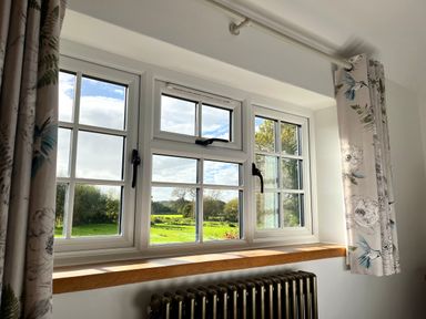 A window with white frames and floral curtains overlooking a green landscape at Old Post Office in Sherborne