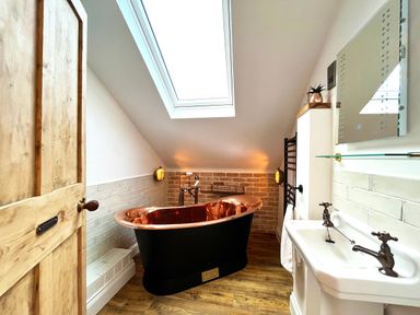 A bathroom with a copper bathtub under a skylight and a sink with taps at Old Post Office Sherborne