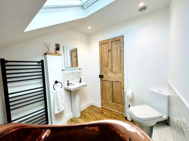 A bathroom with a copper bathtub a pedestal sink a wooden door a toilet and a black towel rack at Old Post Office Sherborne