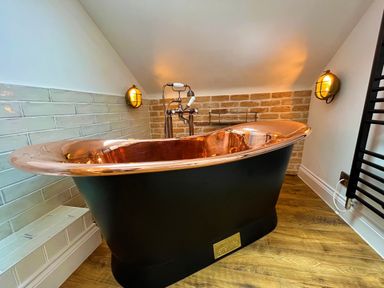A bathroom with a copper and black freestanding bathtub against tiled and brick walls at Old Post Office in Sherborne