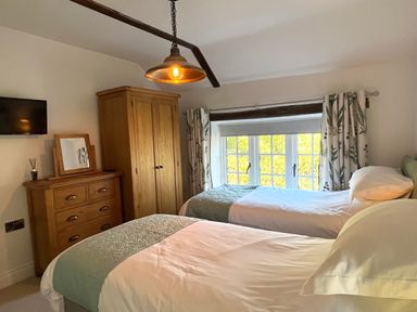 A bedroom with two single beds a wooden dresser wardrobe a wall-mounted TV and a window with curtains at Old Post Office Sherborne