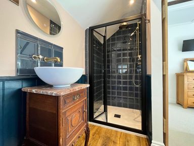 A bathroom with a wooden vanity unit and white basin next to a tiled shower enclosure at Old Post Office in Sherborne