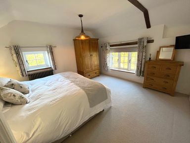 A bedroom with a bed pillows wooden wardrobe wooden chest of drawers and two windows at Old Post Office in Sherborne